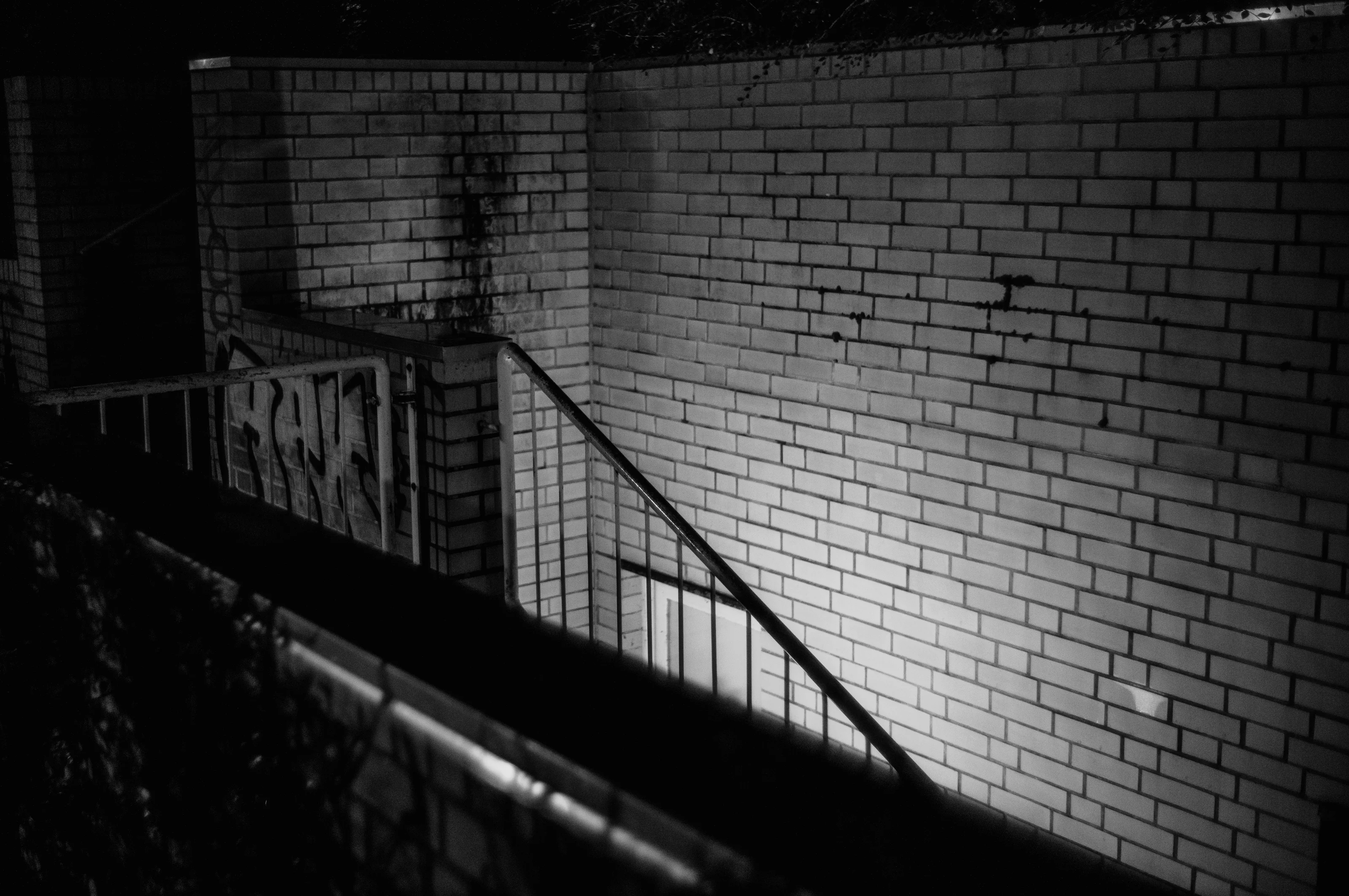 Black and white photo of a dimly lit brick staircase with graffiti.