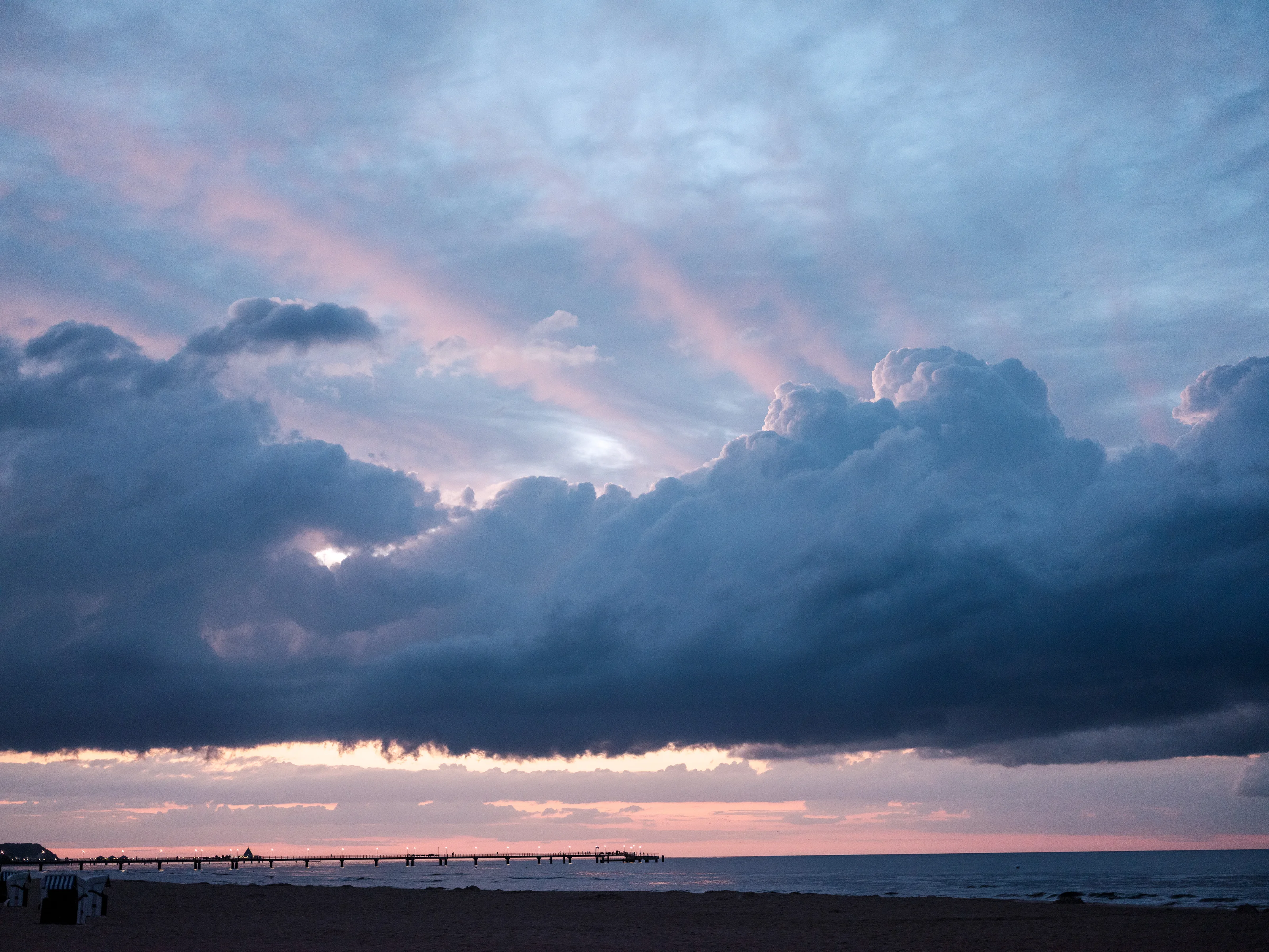 A dramatic beach sunset with large clouds and a pier extending into the sea.