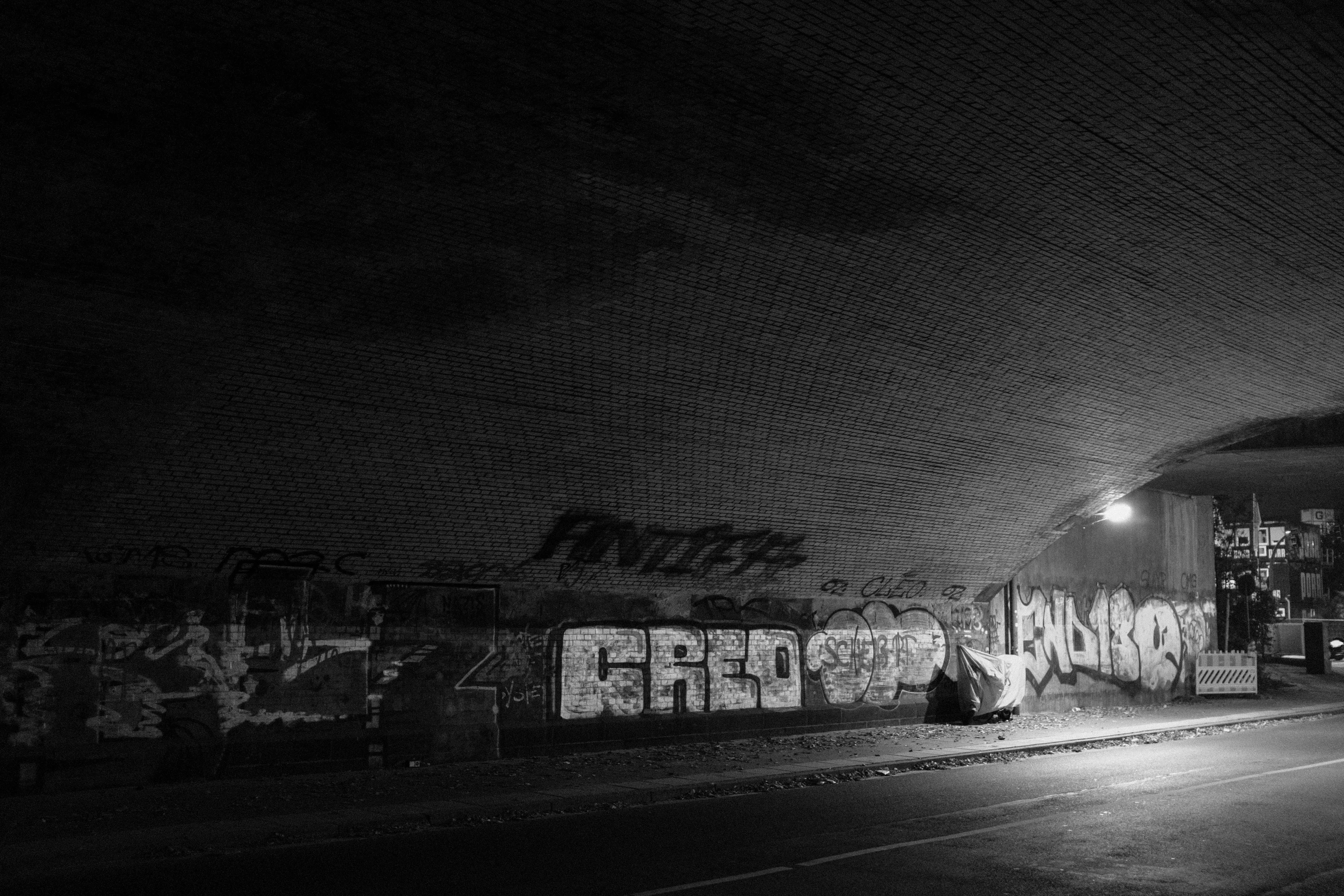 A graffiti-covered underpass with dim lighting and a covered object beneath.
