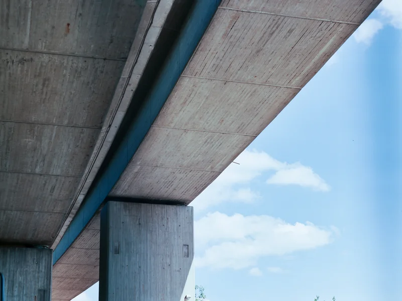 View of an overpass with concrete pillars against a blue sky with clouds.