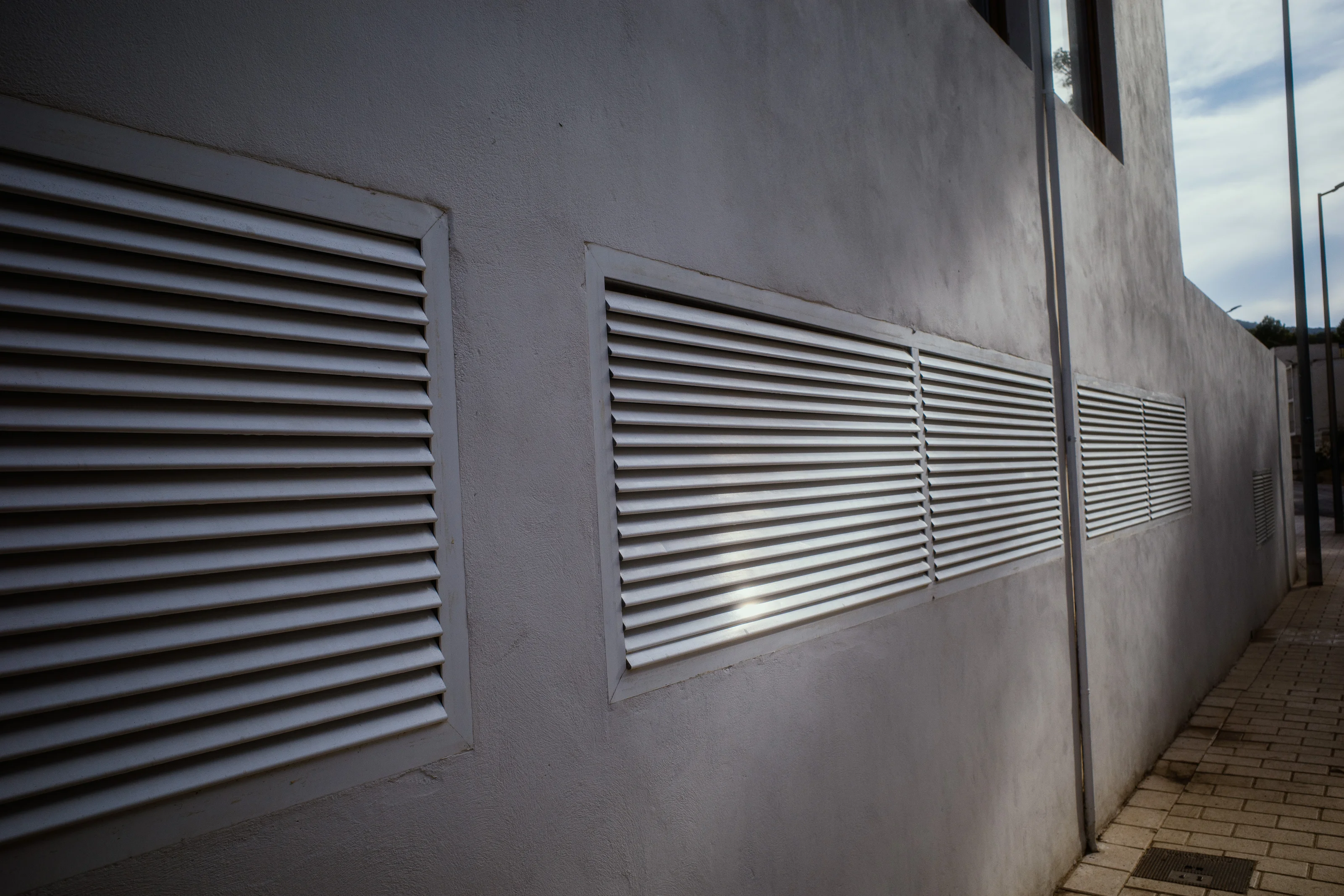 Exterior wall with three horizontal ventilation grilles and a vertical pipe.