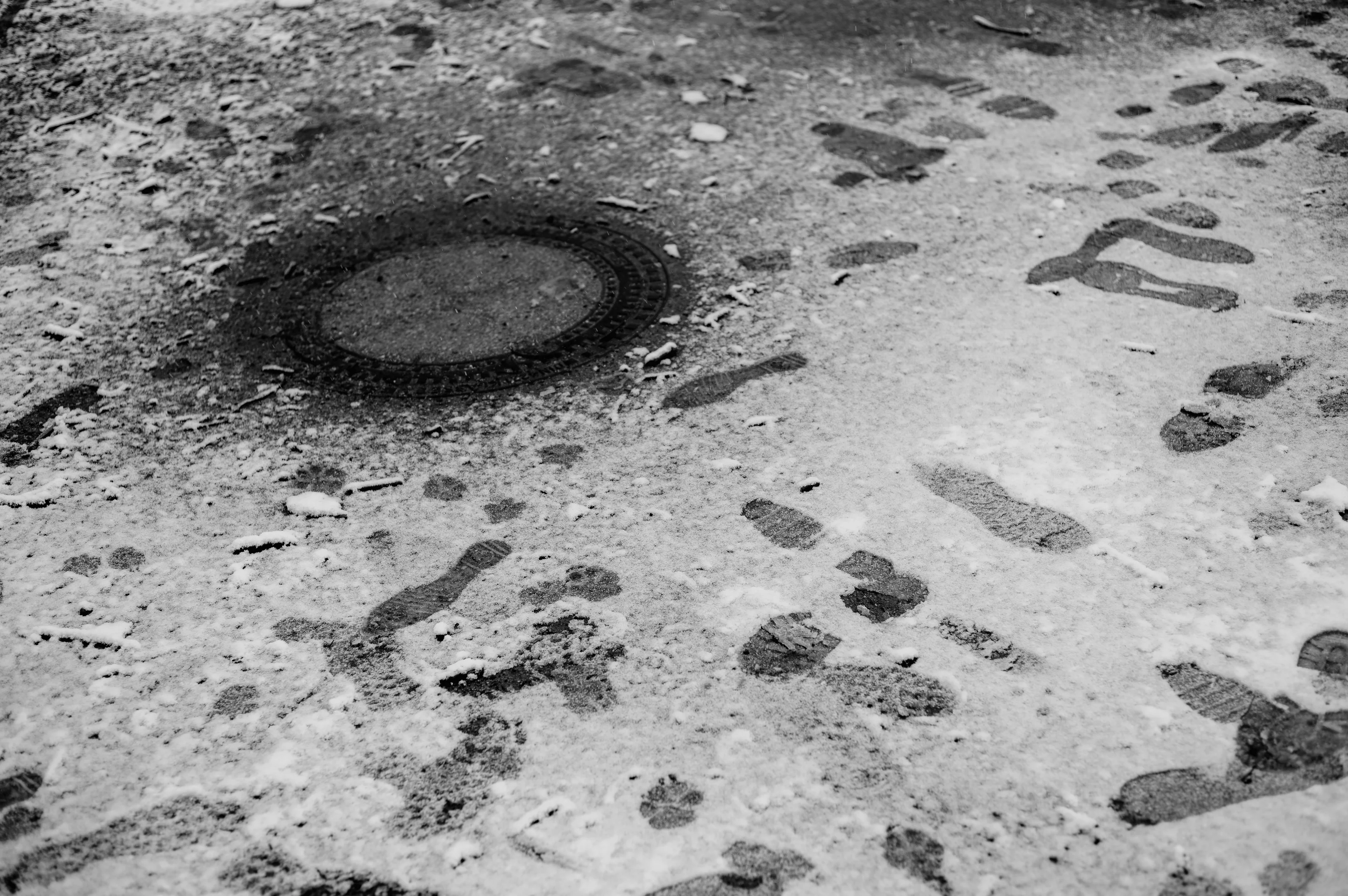 Footprints in the snow surrounding a manhole cover.