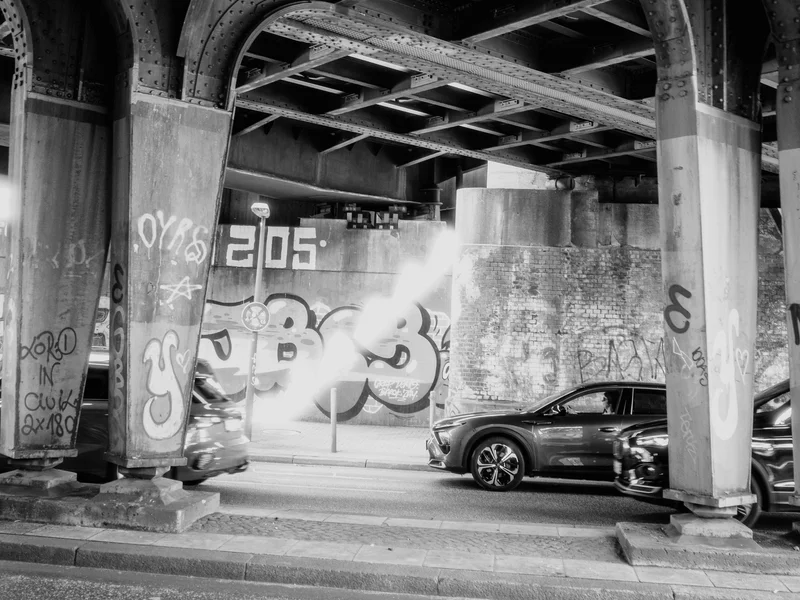 Black and white photo of graffiti-covered underpass with cars passing beneath.