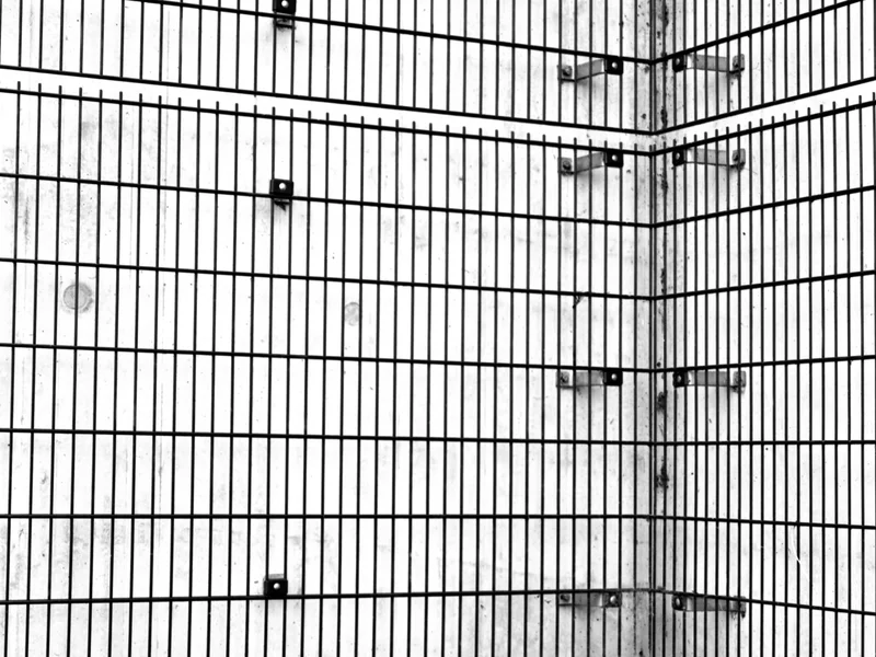 A corner of a concrete wall with vertical black metal bars and some grass at the base.