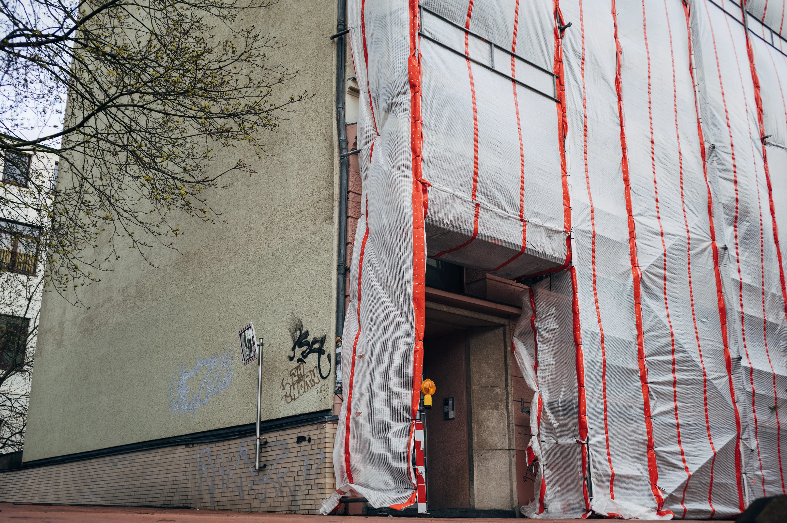Building facade covered with white and red striped protective wrap next to a grafittied wall.