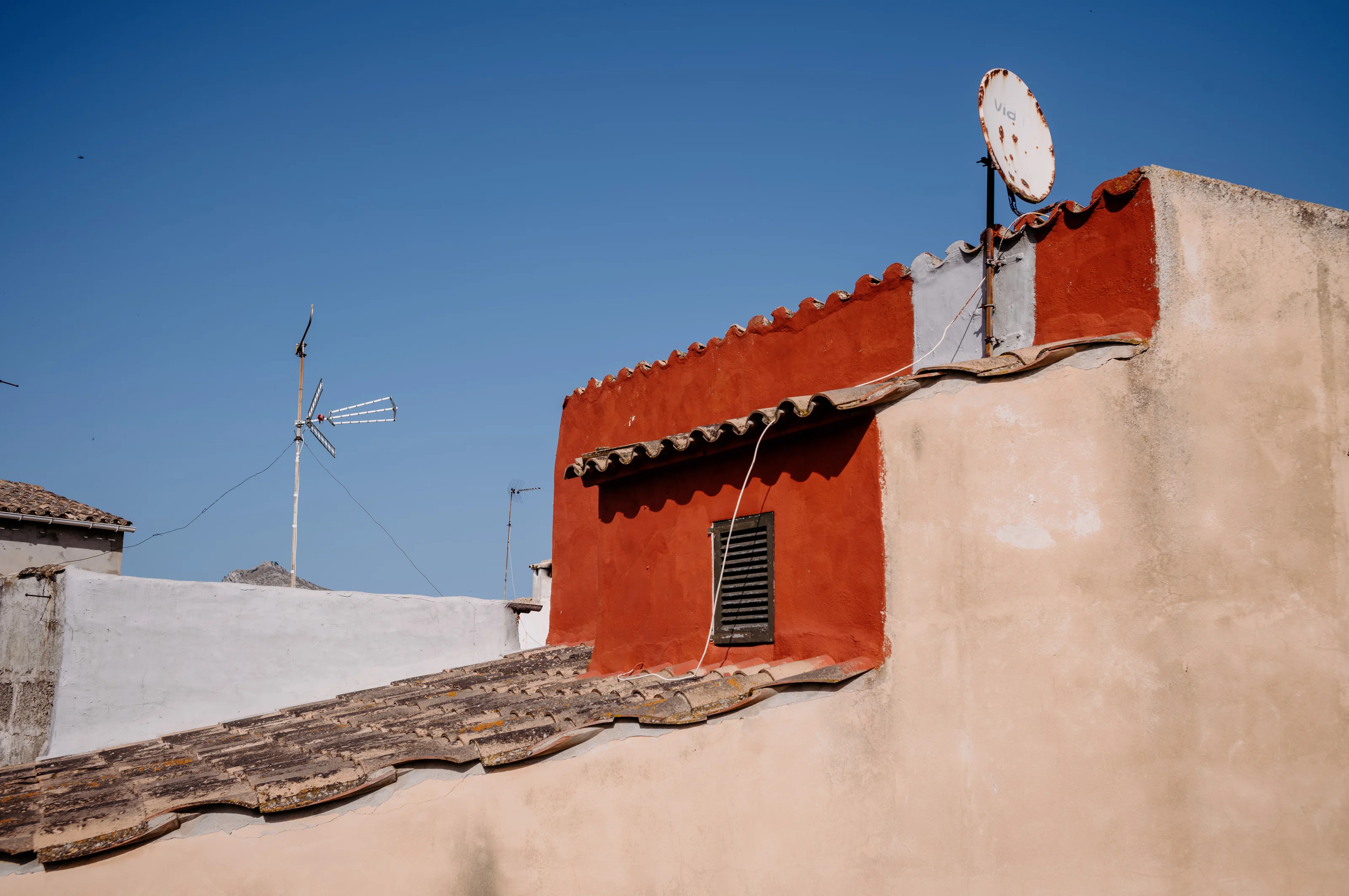 Rustic red-tiled rooftop with satellite dish against a clear blue sky.