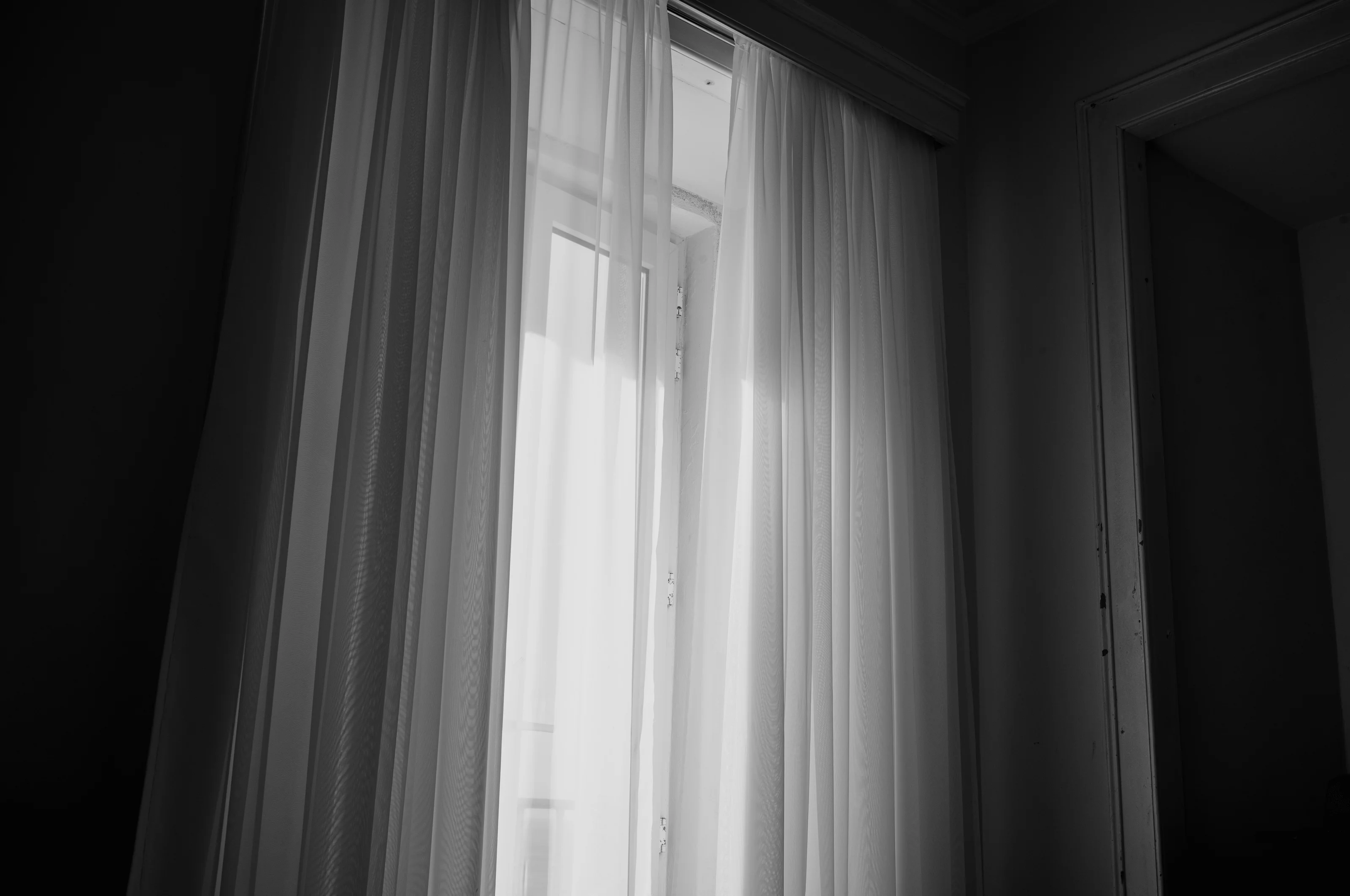 A softly lit window with sheer curtains partially open, letting light in.