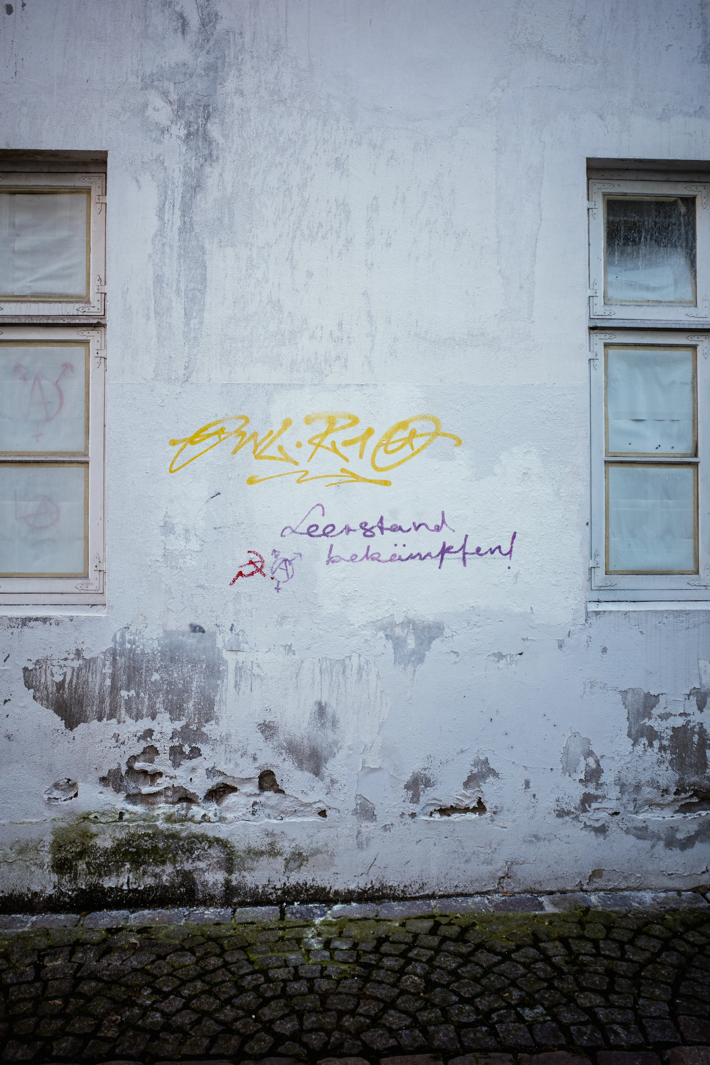 Graffiti on a weathered wall between two windows with cracked paint.