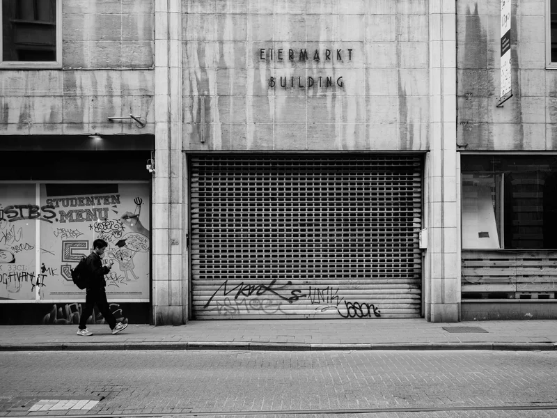 A person walks past a building with a closed shutter and graffiti.