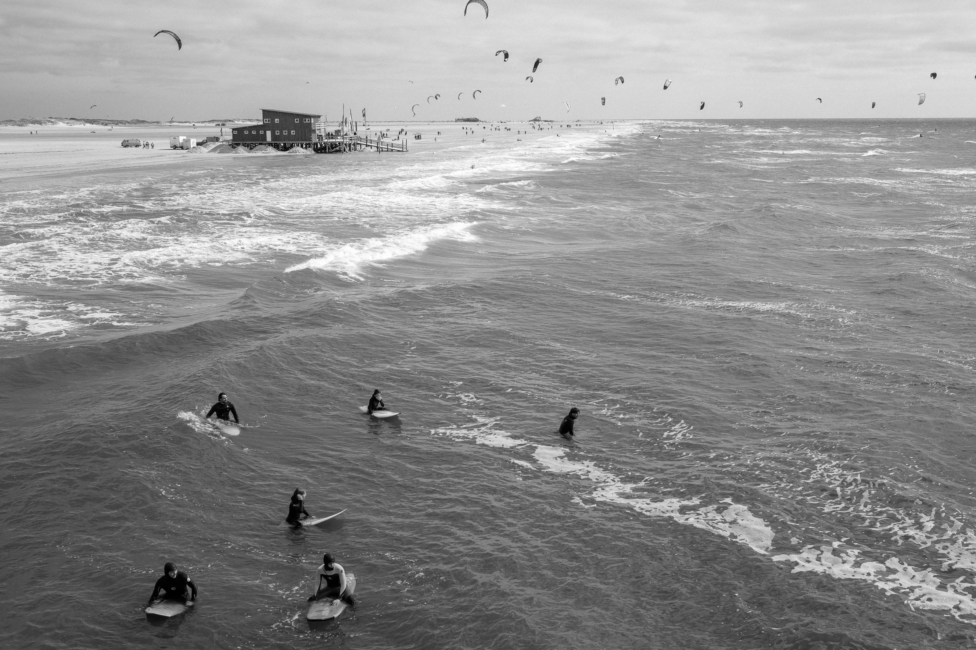 Surfers on the water with a beach in the distance and kites in the sky.