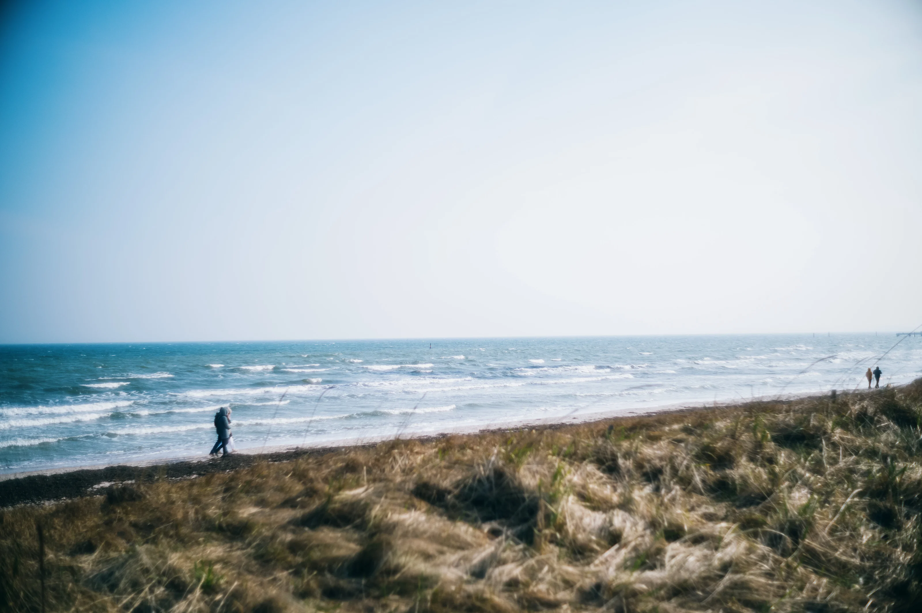 A beach scene with two people walking on the shoreline, with waves in the background under a clear sky.