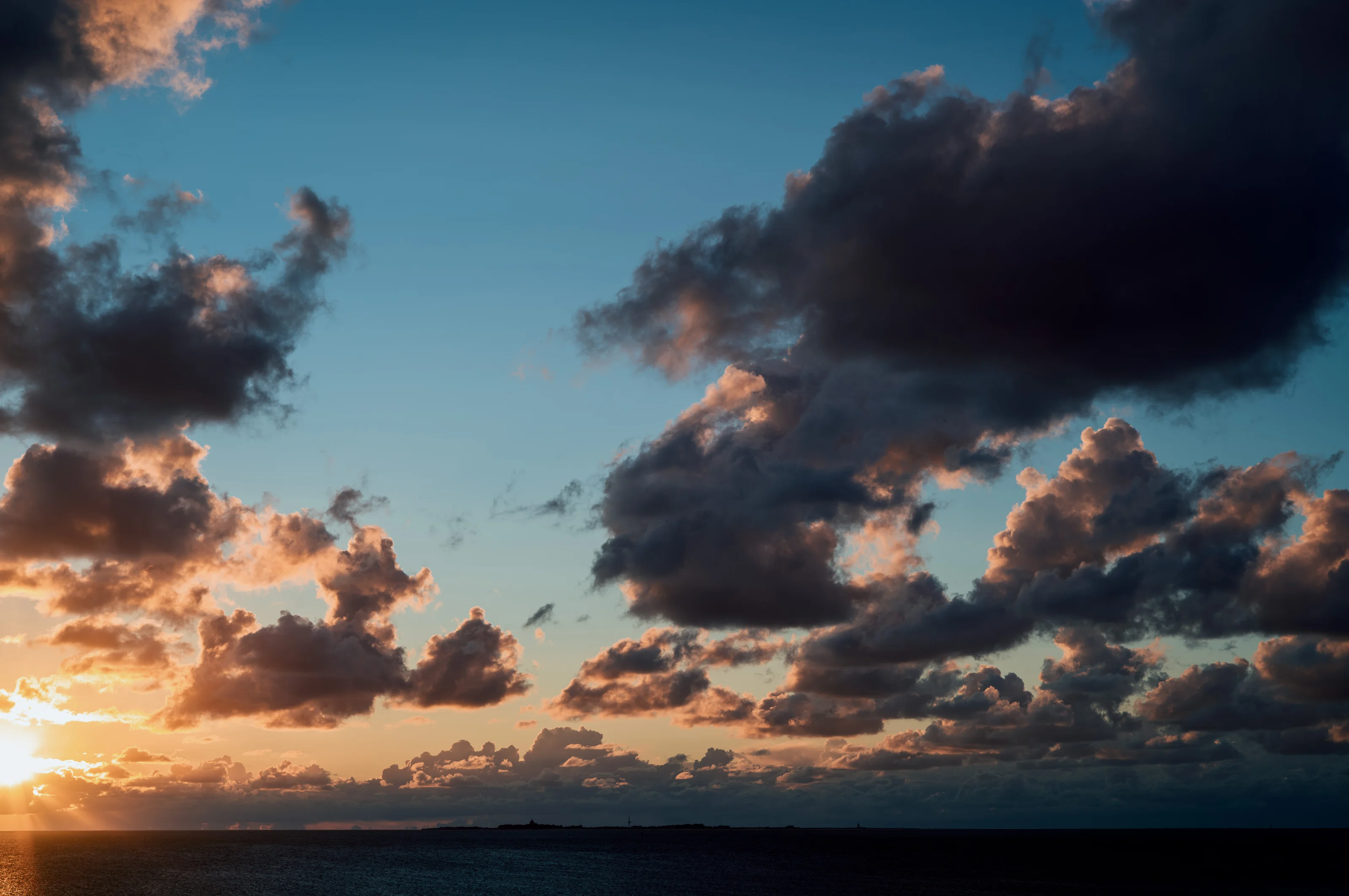Sunset over the ocean with dramatic clouds and a glowing horizon.