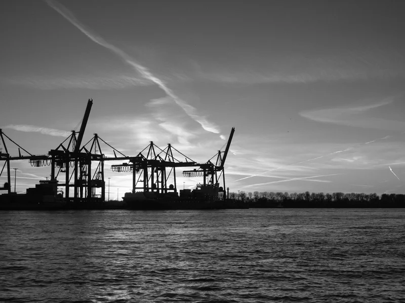 Silhouette of cargo cranes at a port against a dramatic sunset sky.