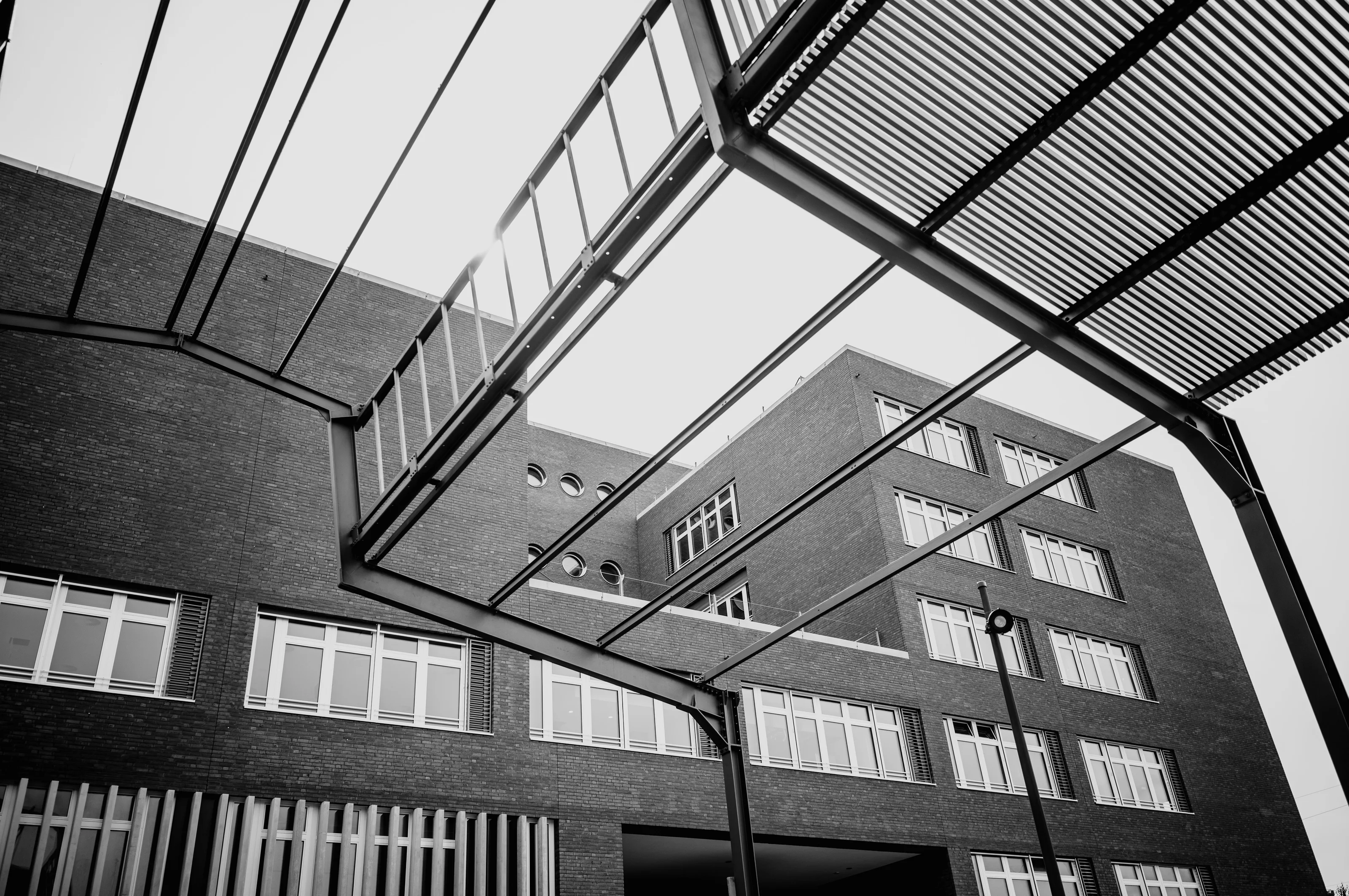 Black and white photograph of a modern brick building with geometric metal frames overhead.