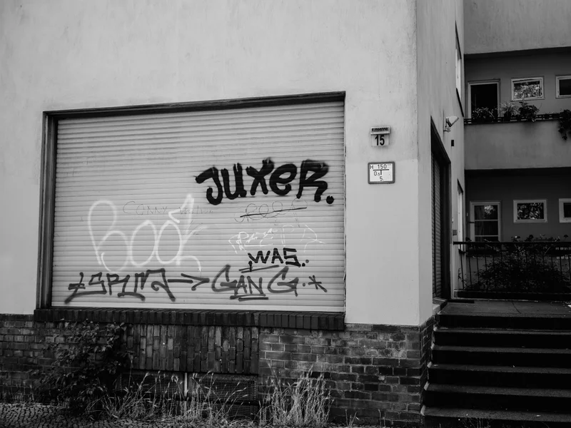 A building facade with graffiti on a roller shutter and adjacent staircase.