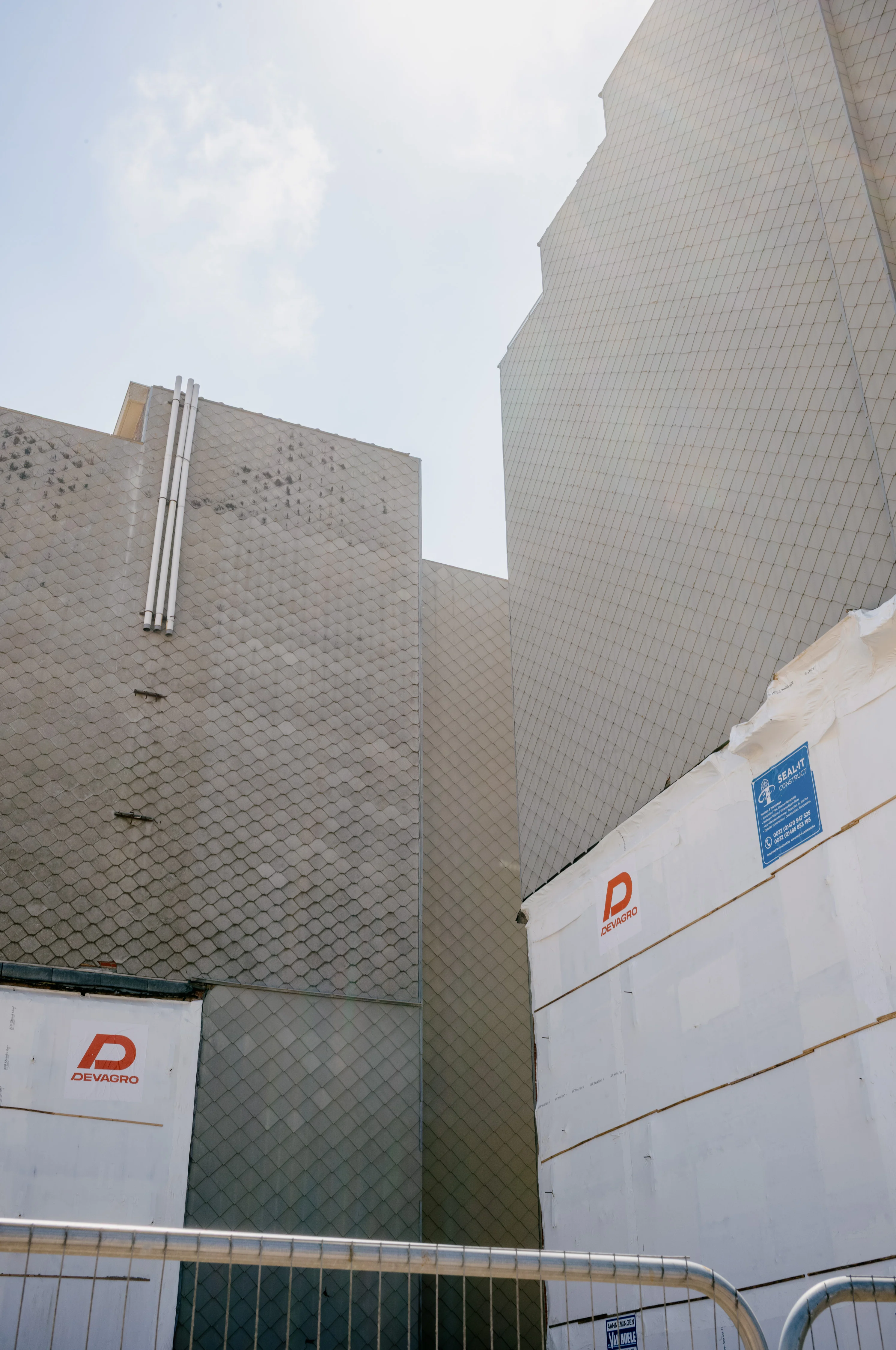 Tall gray tiled buildings with construction signs under a partly cloudy sky.