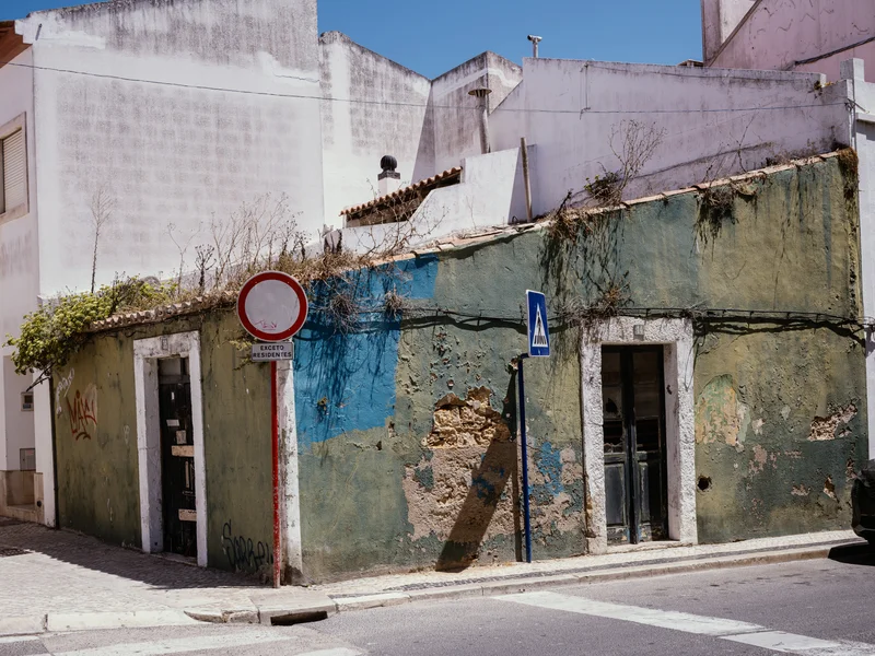 A worn, colorful wall of a building with a round traffic sign and a pedestrian crossing sign in an urban setting.