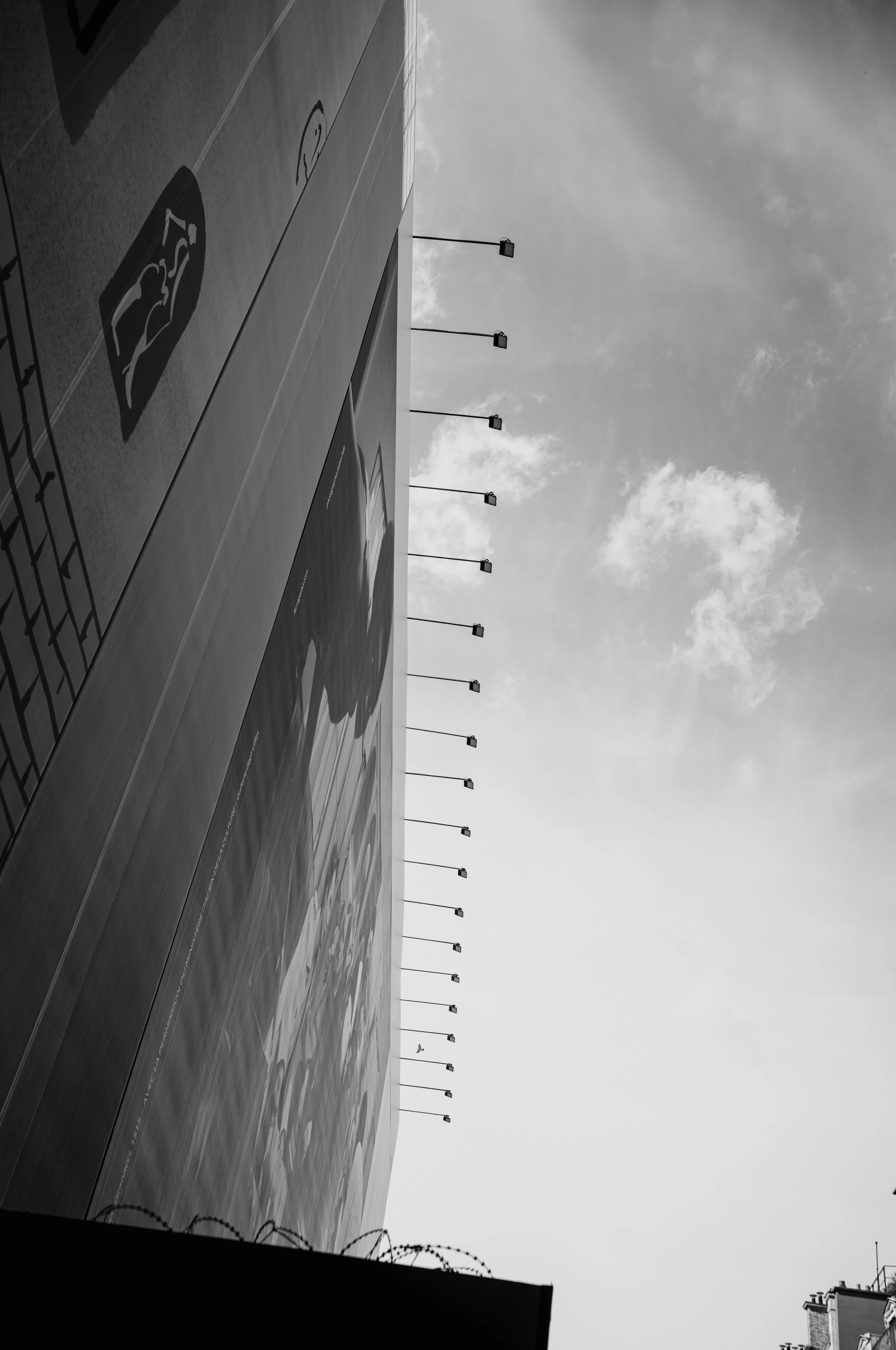 Side view of a large building with wall lamps extending outward, against a cloudy sky.