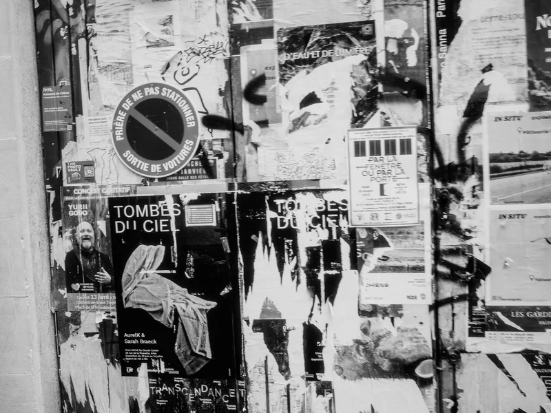 Black and white photo of a wooden door covered with various torn posters and graffiti.