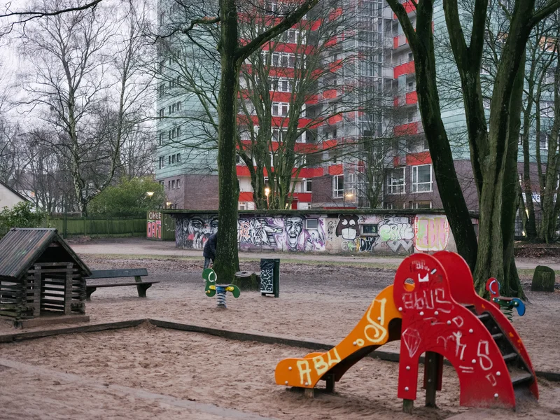 Urban playground with colorful slide, trees, and graffiti-covered wall beside a tall residential building.