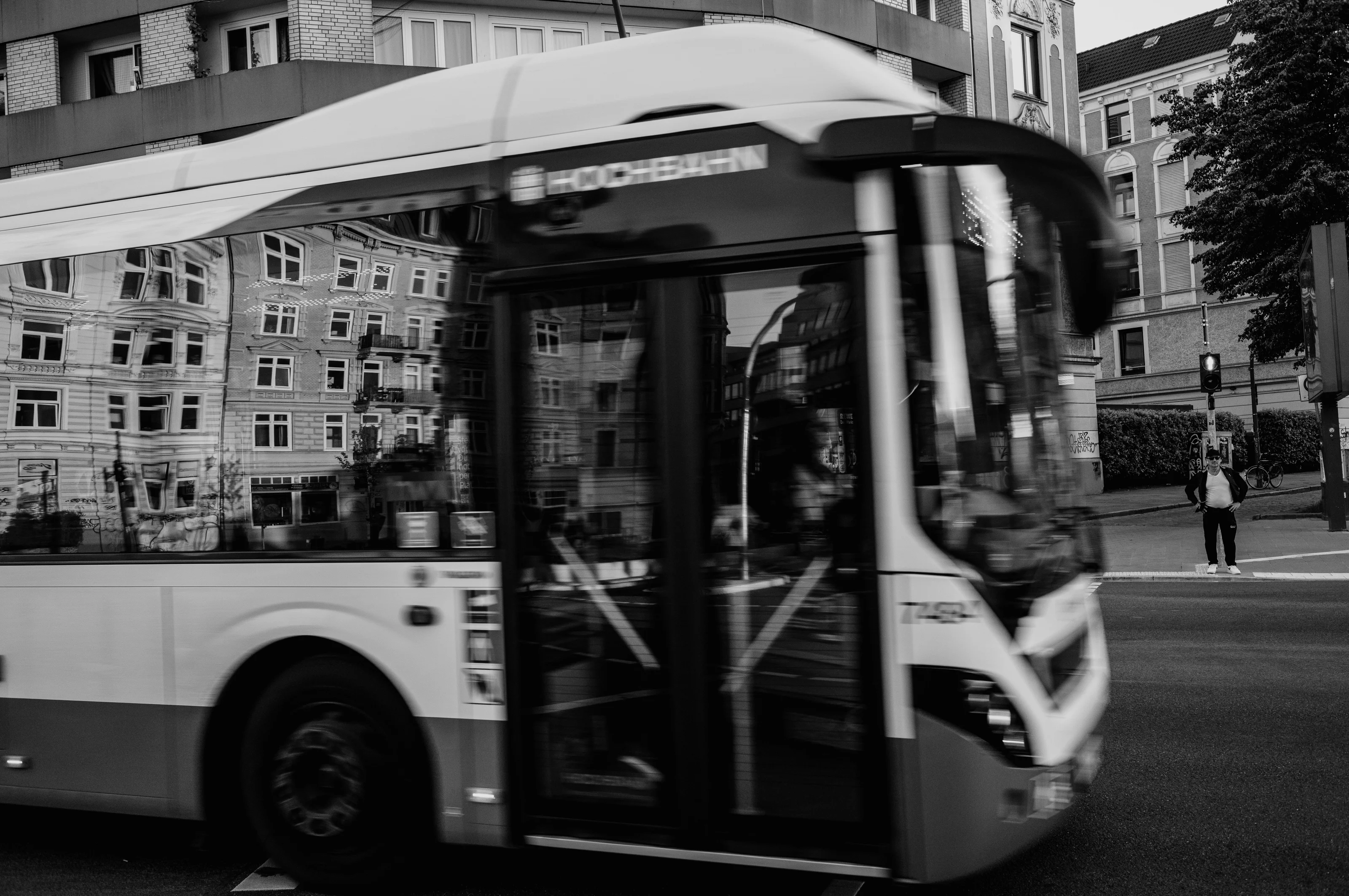 A black and white photo of a bus in motion with a reflection of a building on its windows.