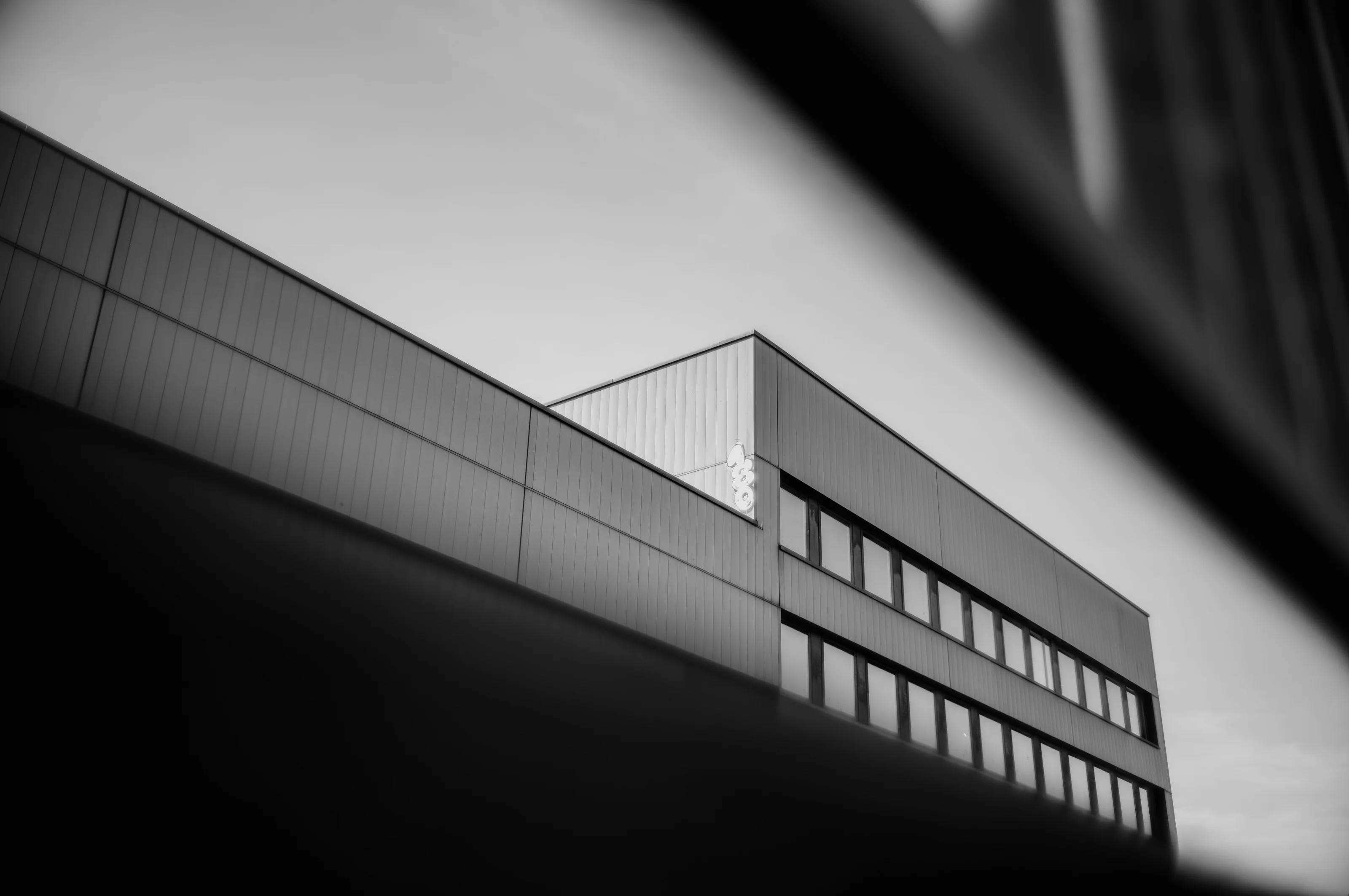 Black and white image of a modern building with multiple large windows and a partially visible sign.