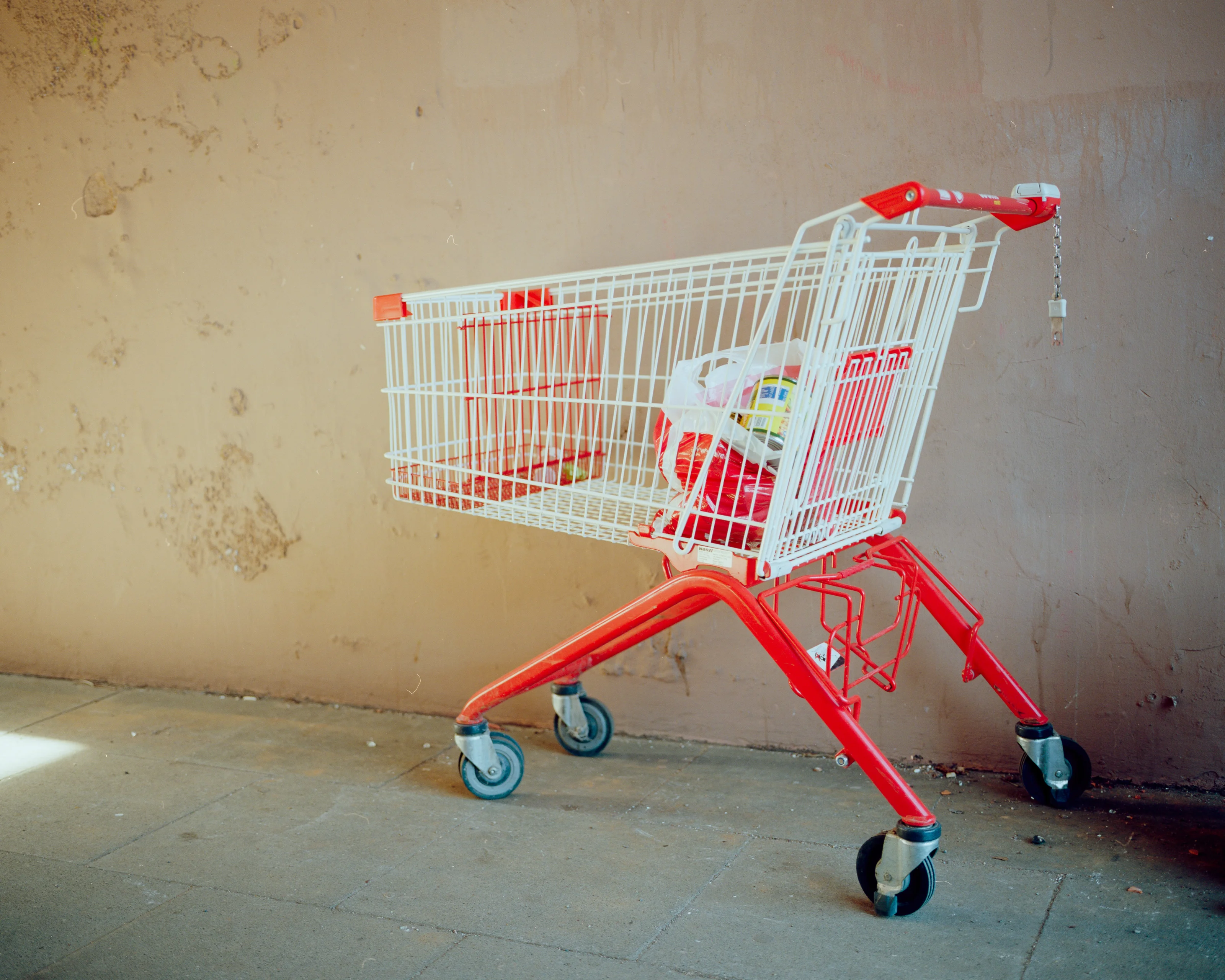 A red and white shopping cart filled with items against a textured wall.