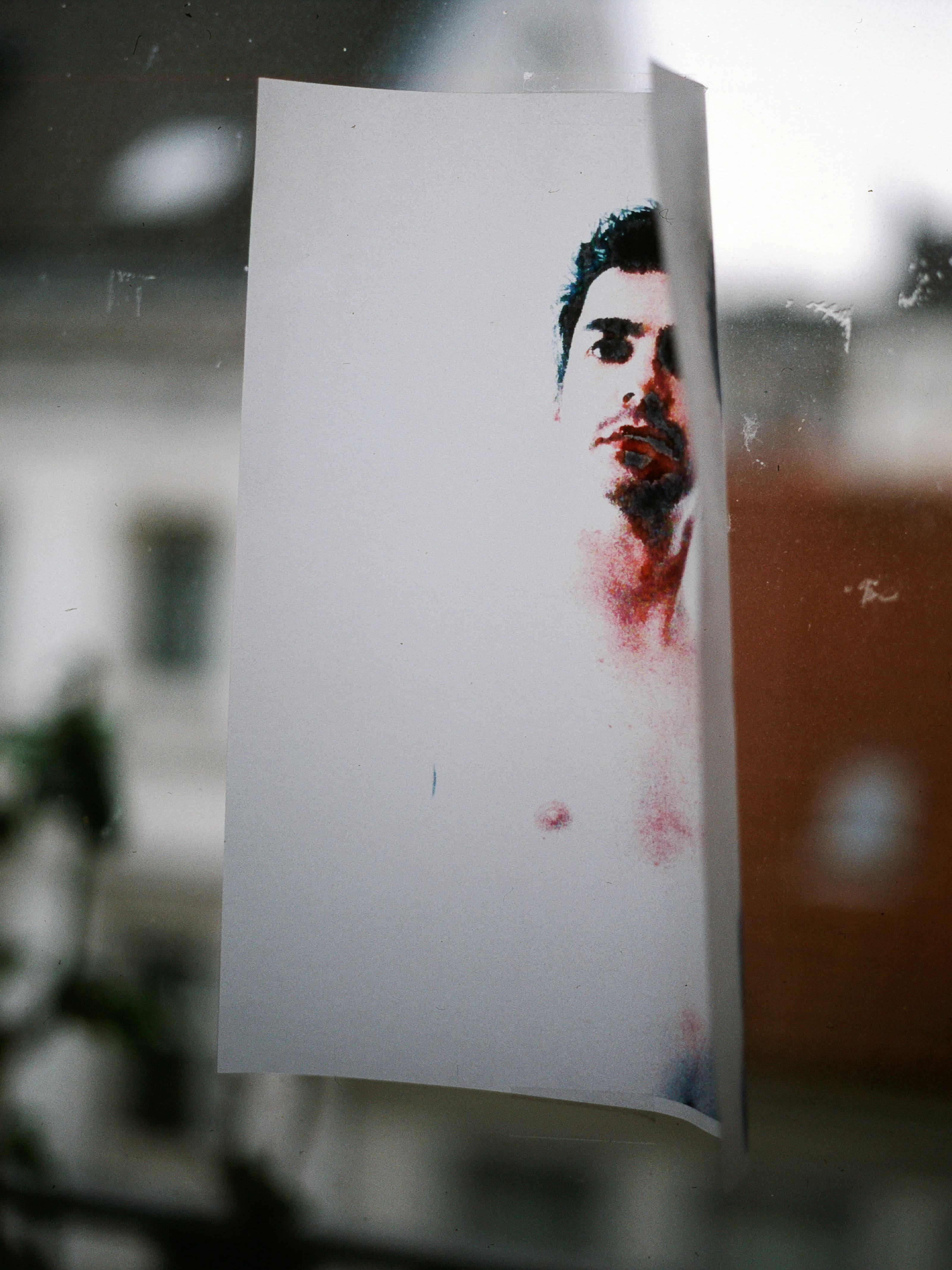 A photo of a printed portrait taped to a window with an urban backdrop.
