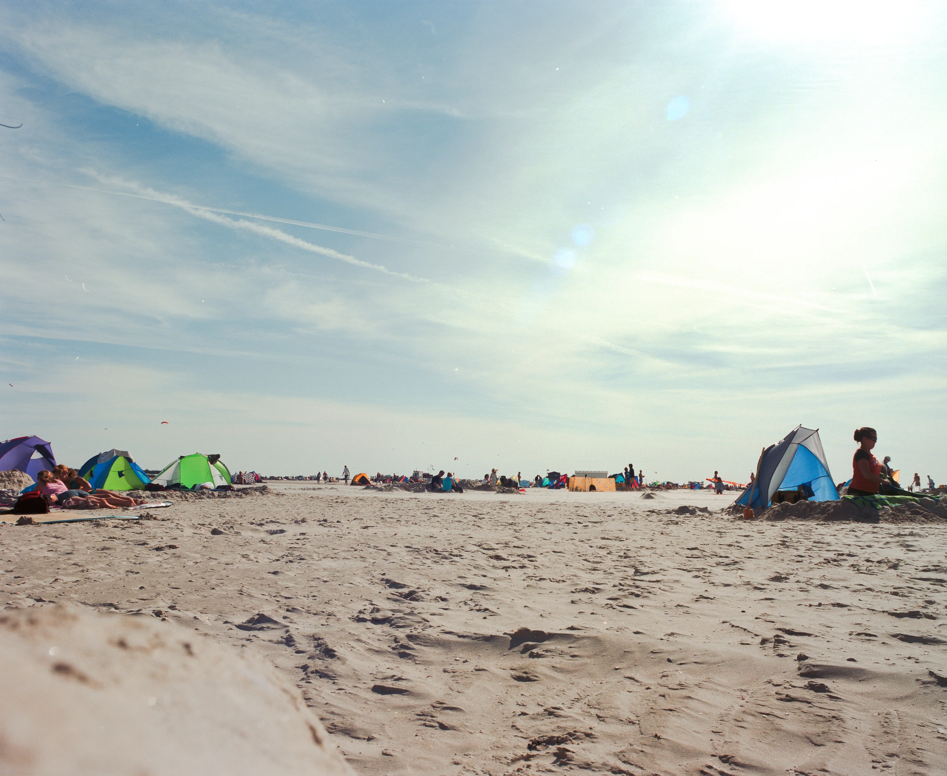 People relaxing under tents on a sandy beach with a bright sky overhead.