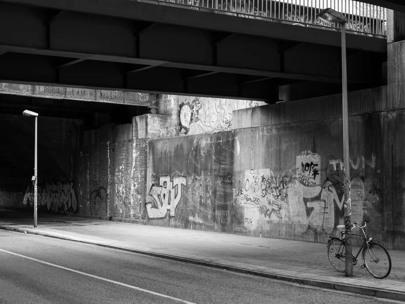 Black and white photo of a graffiti-covered underpass with a bicycle leaned against a lamp post.